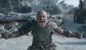 Baraka (C.J. Bloomfield) an armored man with way too many teeth stands in front of a village and skulls mounted on spikes in Mortal Kombat 2.